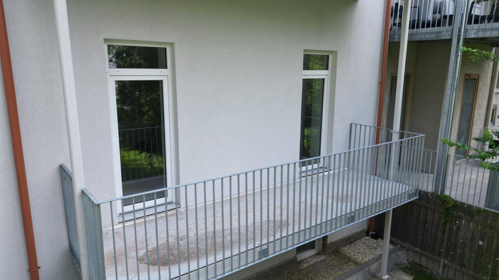 Neuer Balkon mit Metallgeländer an der Gebäudefassade, umgeben von Grün.