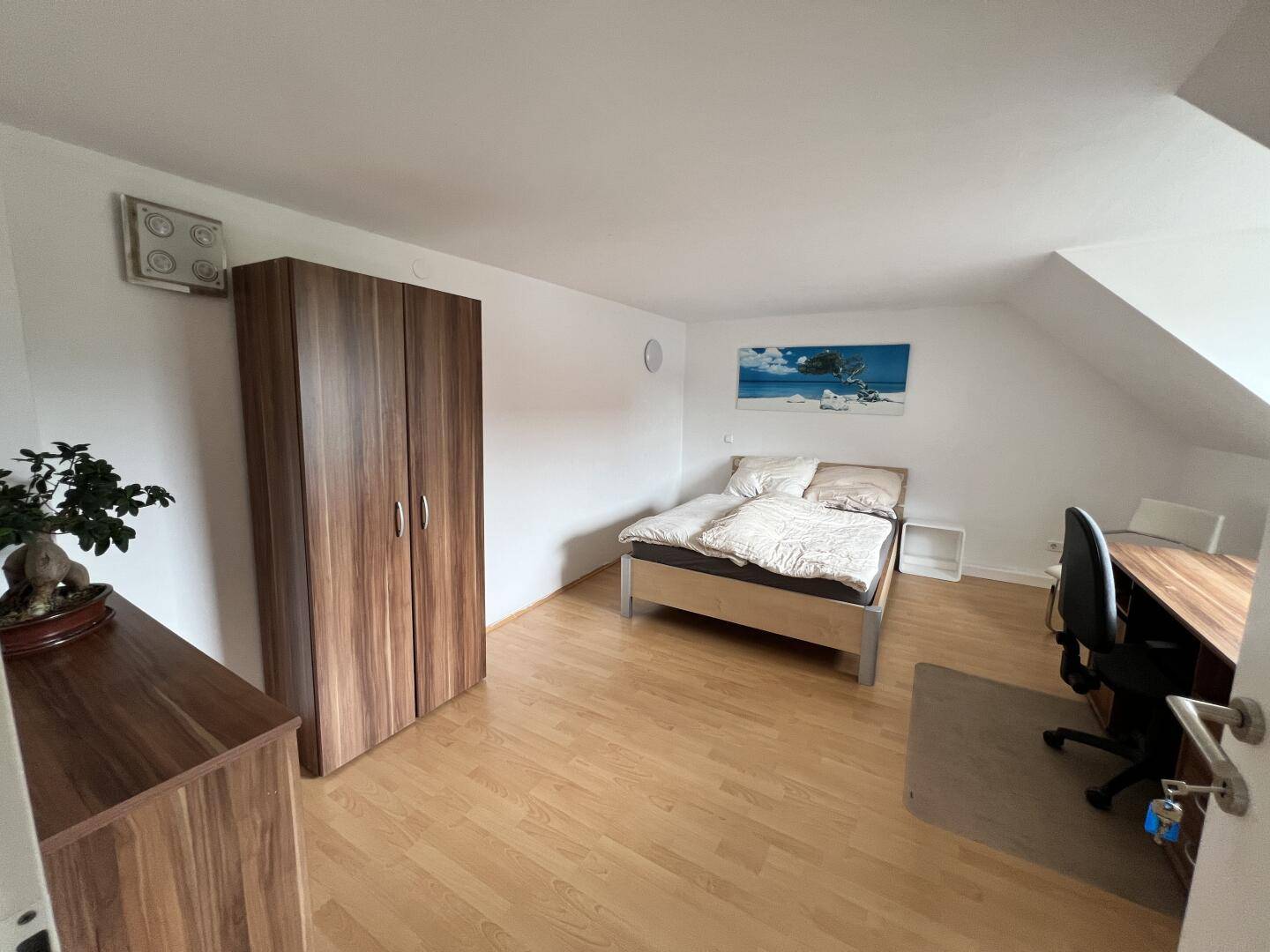 Helles Schlafzimmer mit Holzboden, großem Kleiderschrank und einem bequemen Bett im Dachgeschoss.