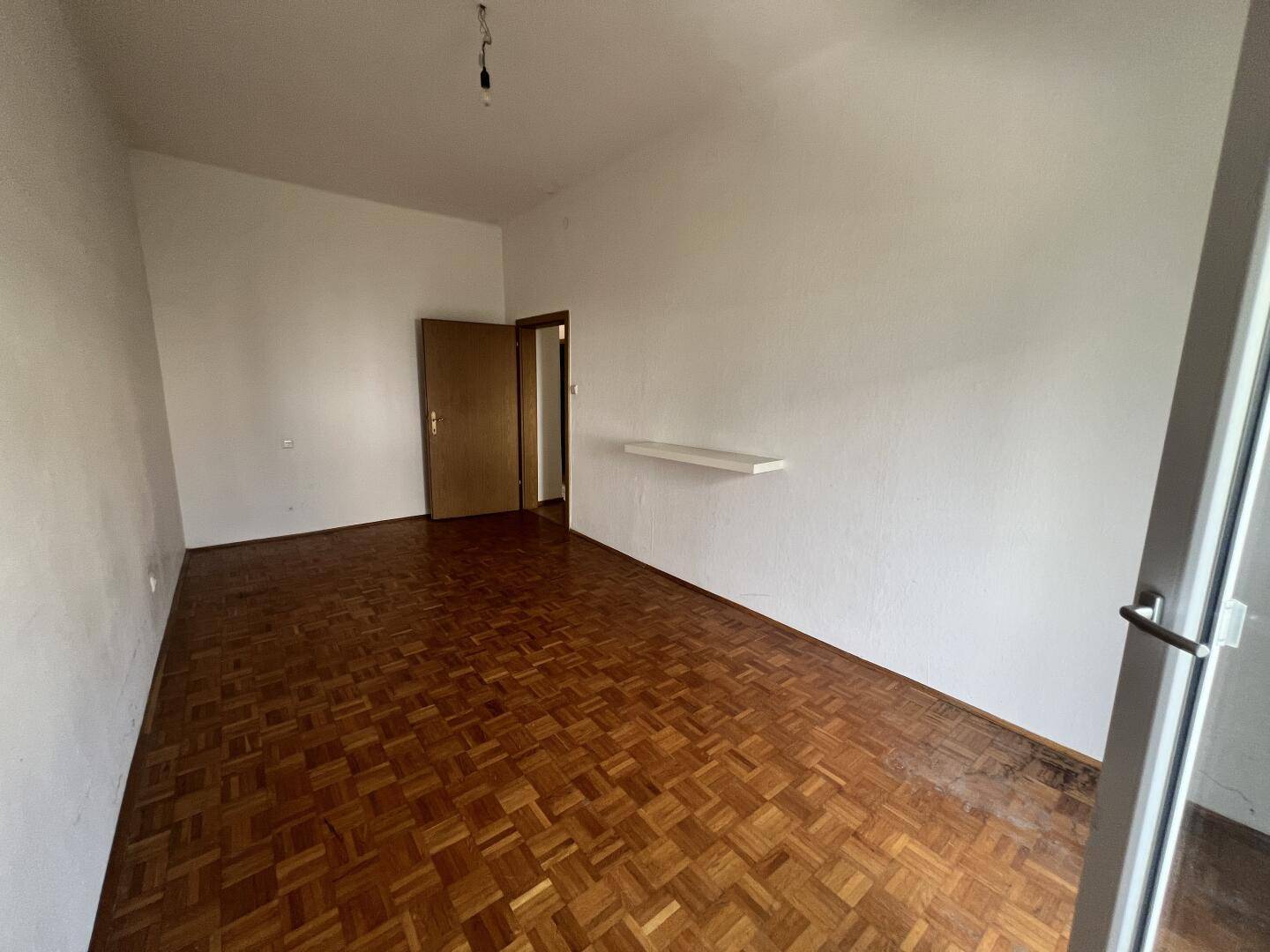 Helles Zimmer mit Parkettboden und einfacher Wanddekoration, ideal für Schlafzimmer.