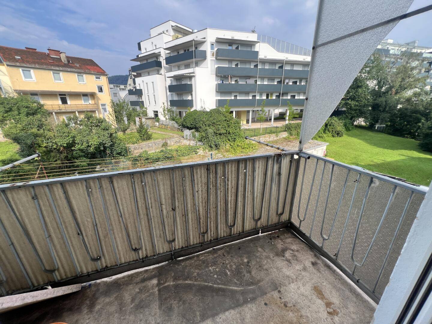 Balkon mit Metallgeländer und Blick auf die umliegenden Gebäude und Grünflächen.