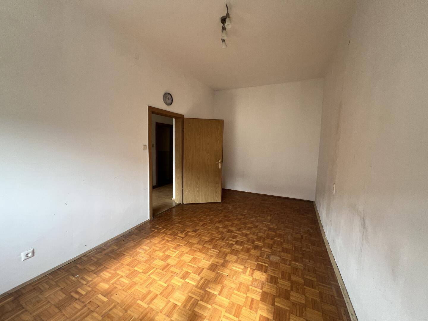 Helles Zimmer mit Parkettboden und Holztür, vielseitig nutzbar als Schlaf- oder Arbeitszimmer.