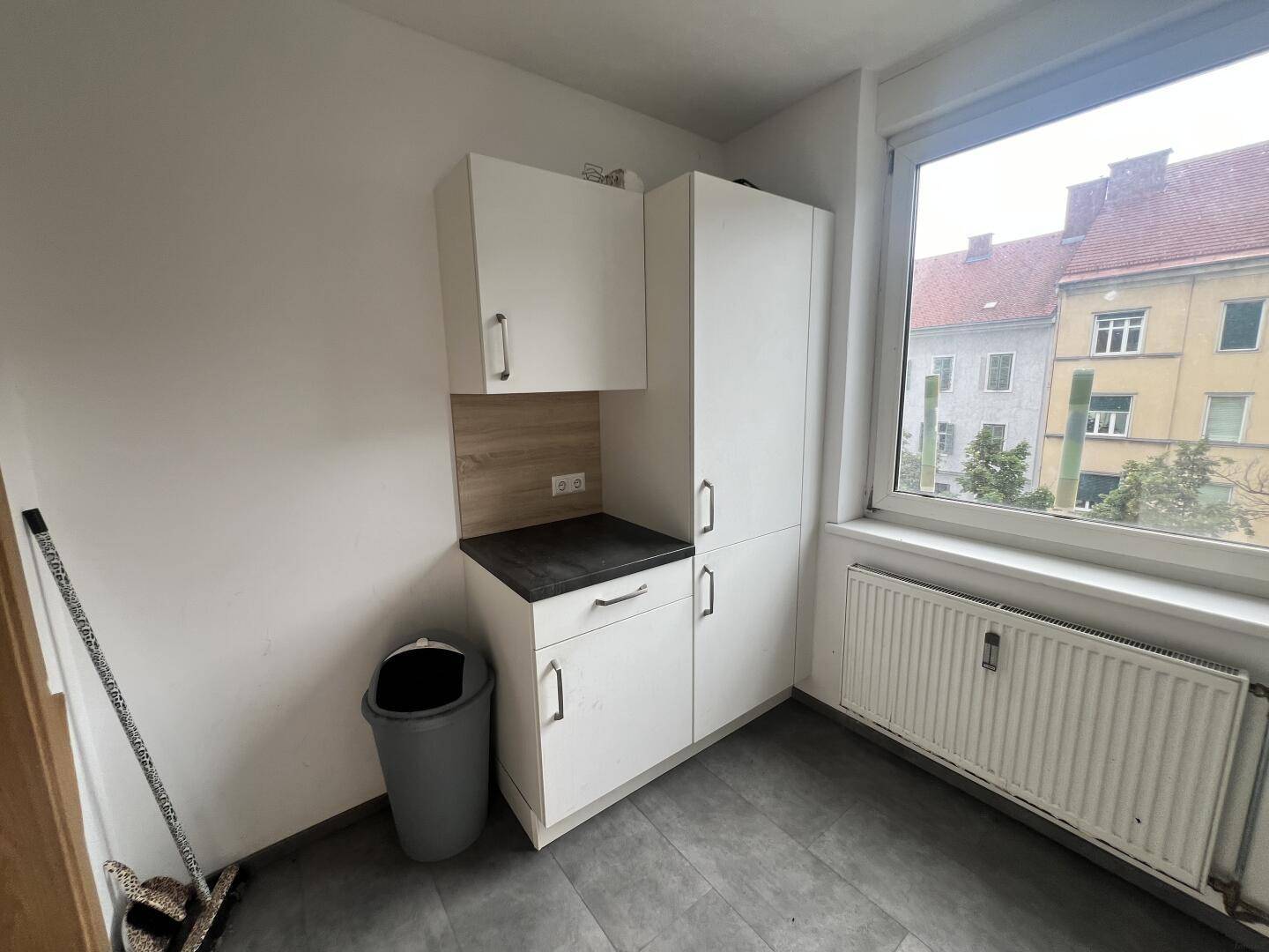 Kleiner Abstellraum oder Küchenzeile mit Schränken, Arbeitsplatte und Fenster.