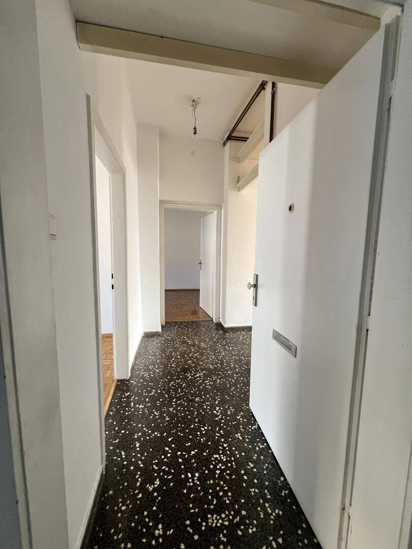 Heller Eingangsbereich mit dunklem Terrazzoboden und weißen Wänden, der zu weiteren Räumen führt.