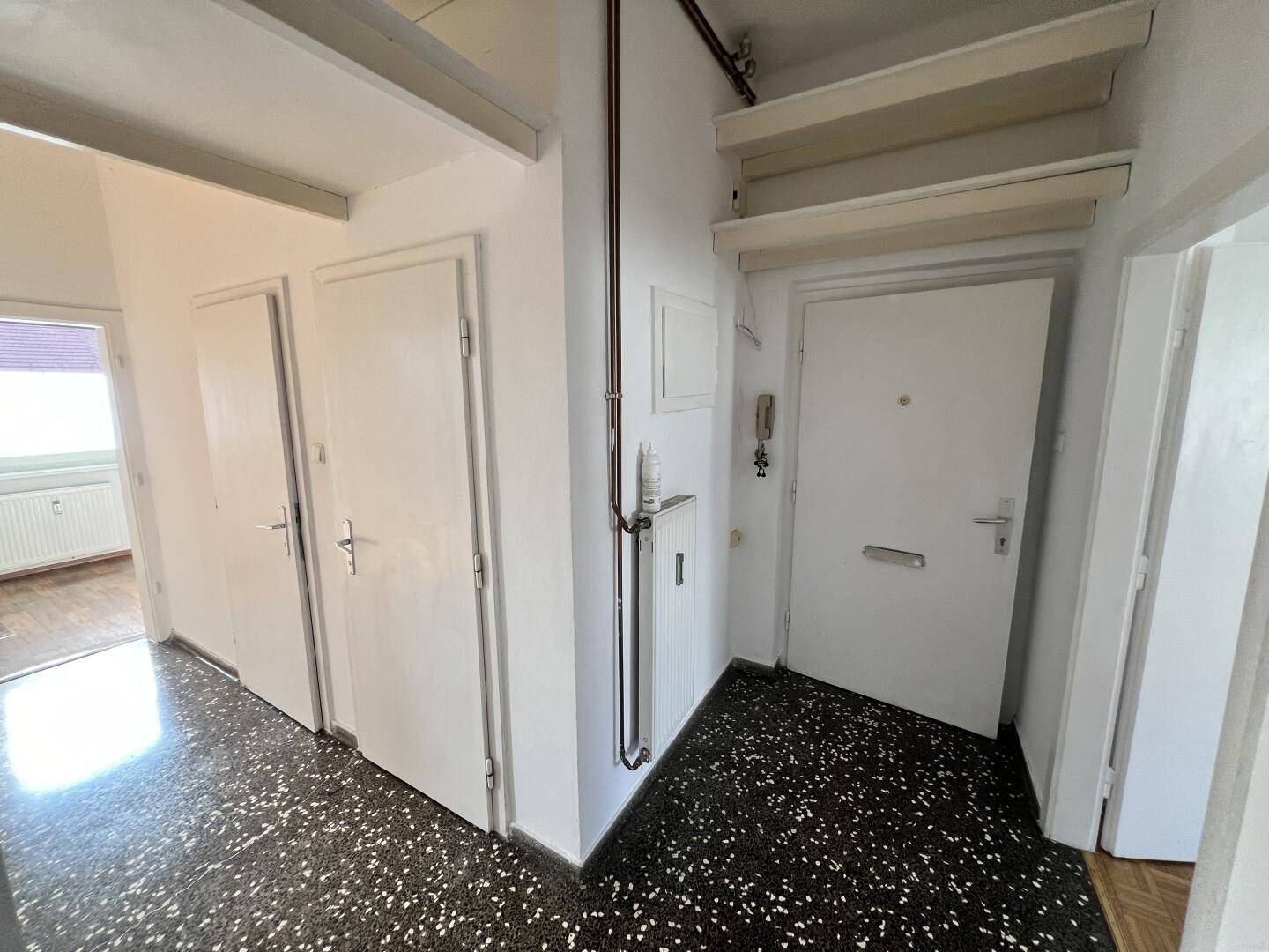 Langer Flur mit dunklem Fliesenboden, weißen Türen und einer Gegensprechanlage.