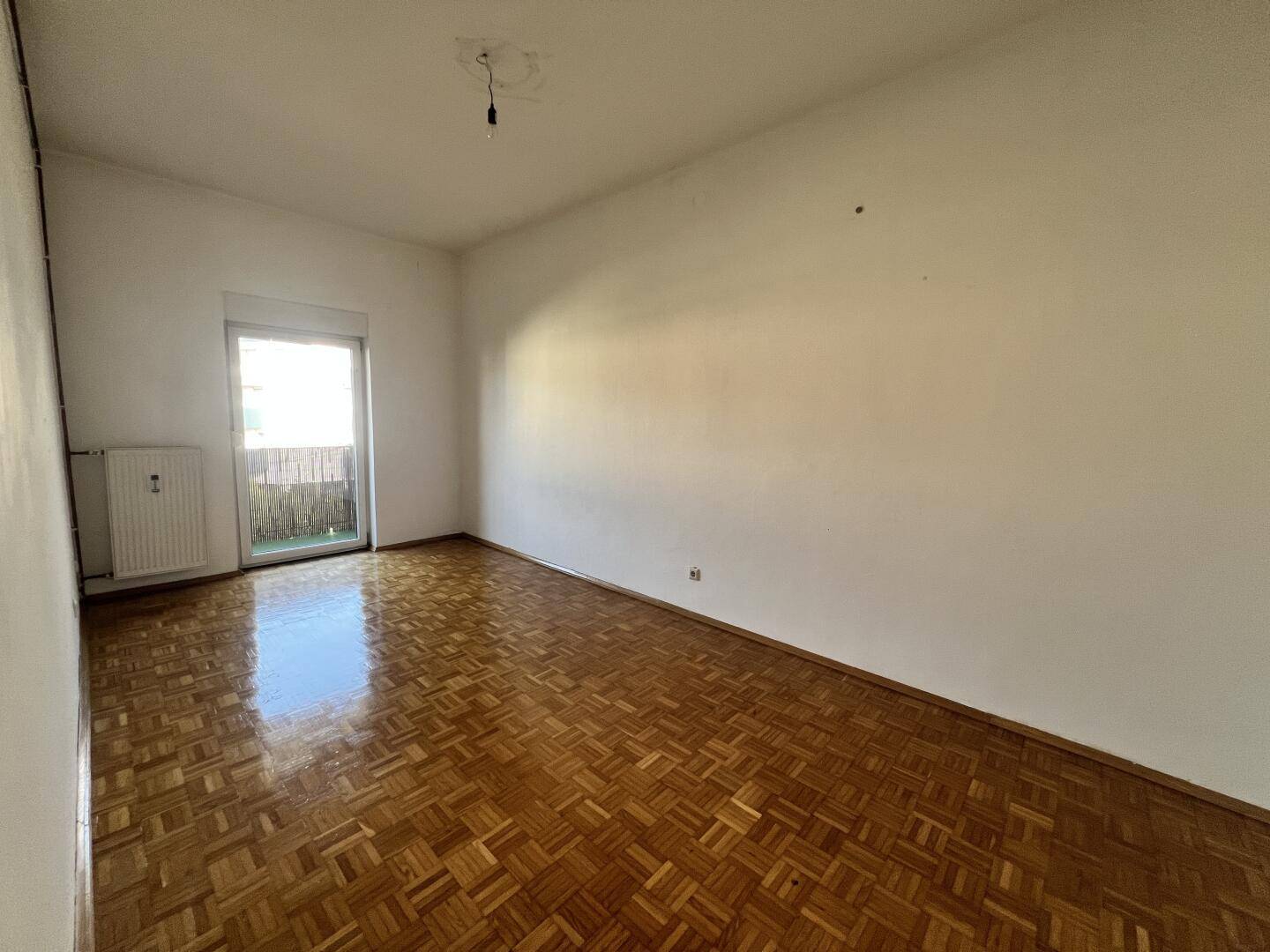 Helles Wohnzimmer mit Parkettboden und direktem Zugang zu einem Balkon.