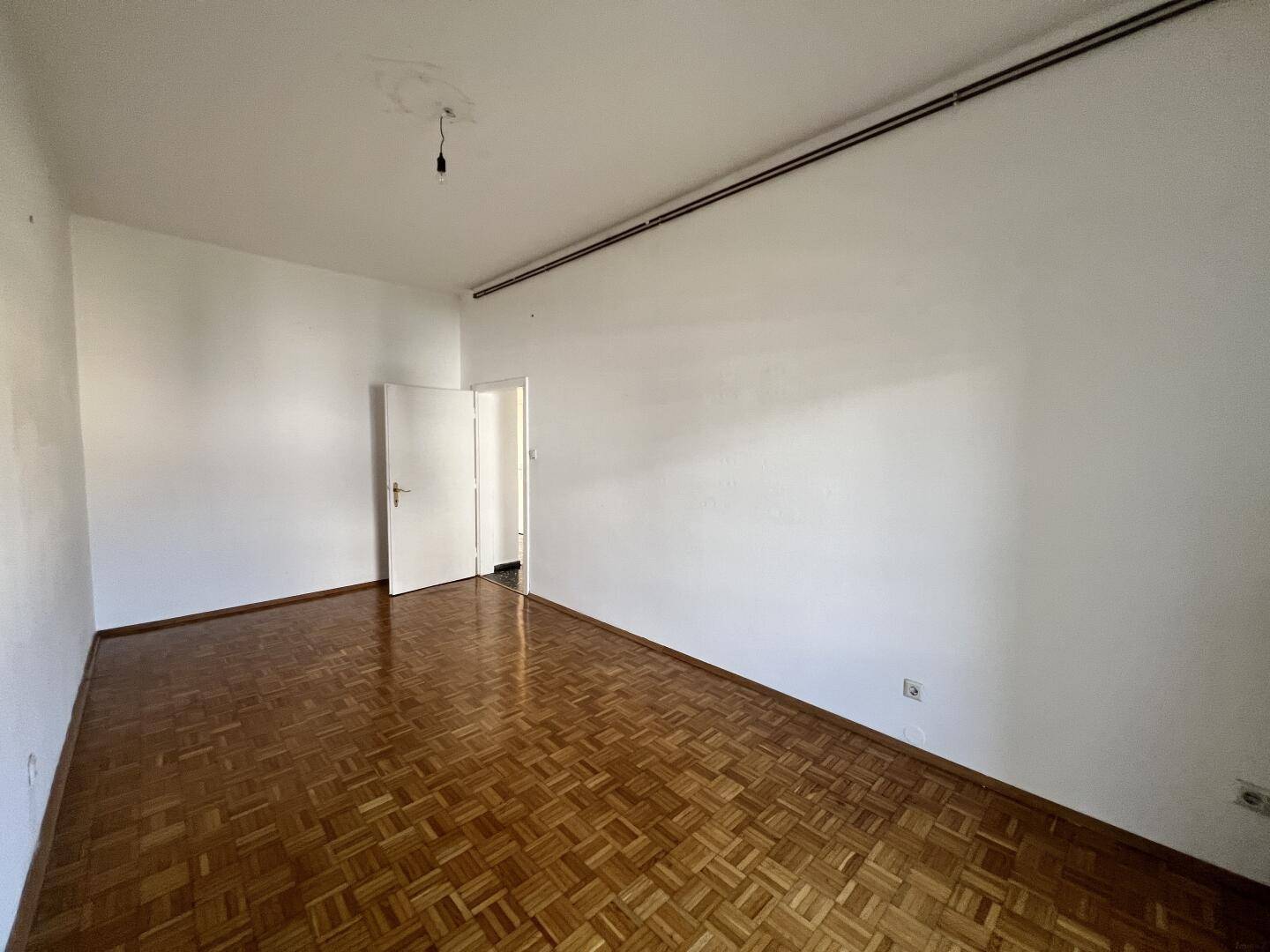 Geräumiges Wohnzimmer mit glänzendem Parkettboden und viel Tageslicht.