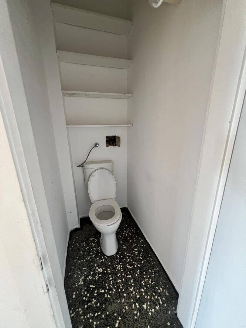 Kleines separates WC mit Toilette, weißen Wänden und dunklem Fliesenboden.