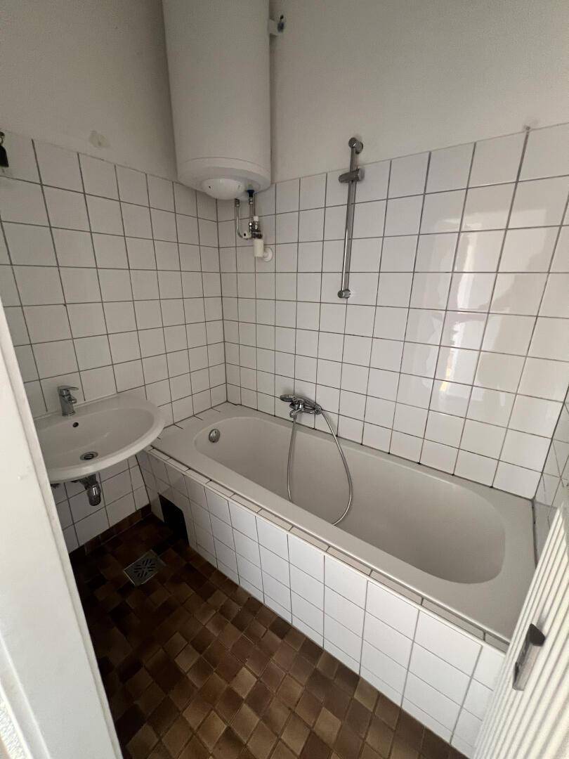 Badezimmer mit Badewanne, Waschbecken, weißen Wandfliesen und braunem Boden.