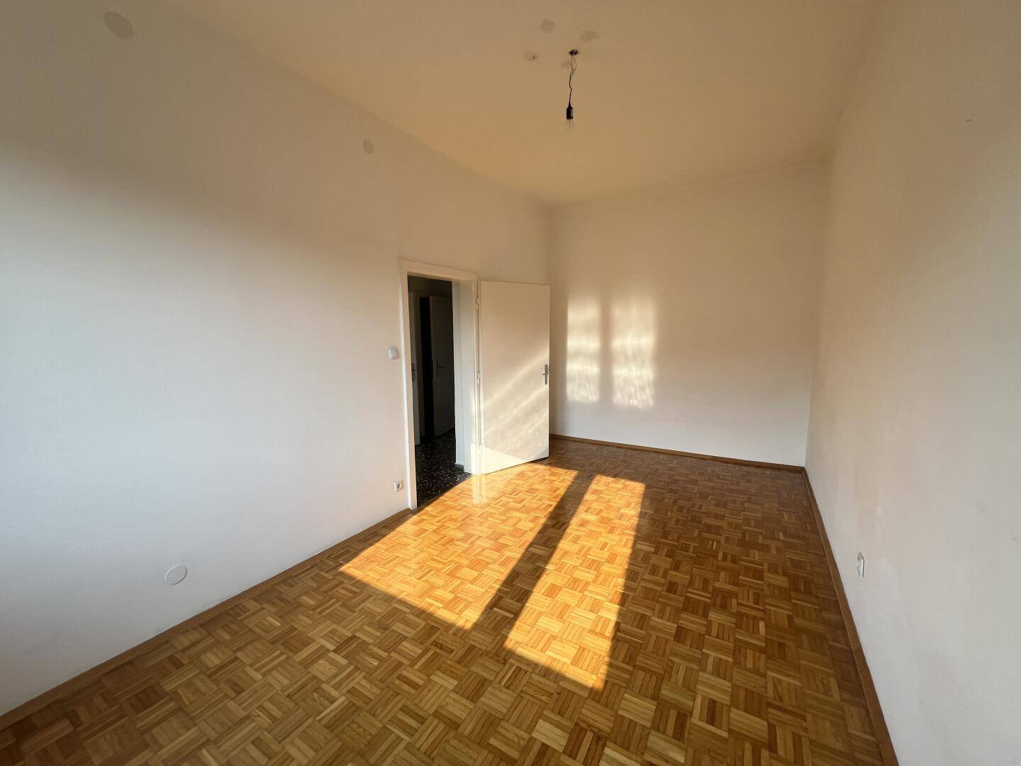 Helles Zimmer mit glänzendem Parkettboden, das von der Sonne durchflutet wird.