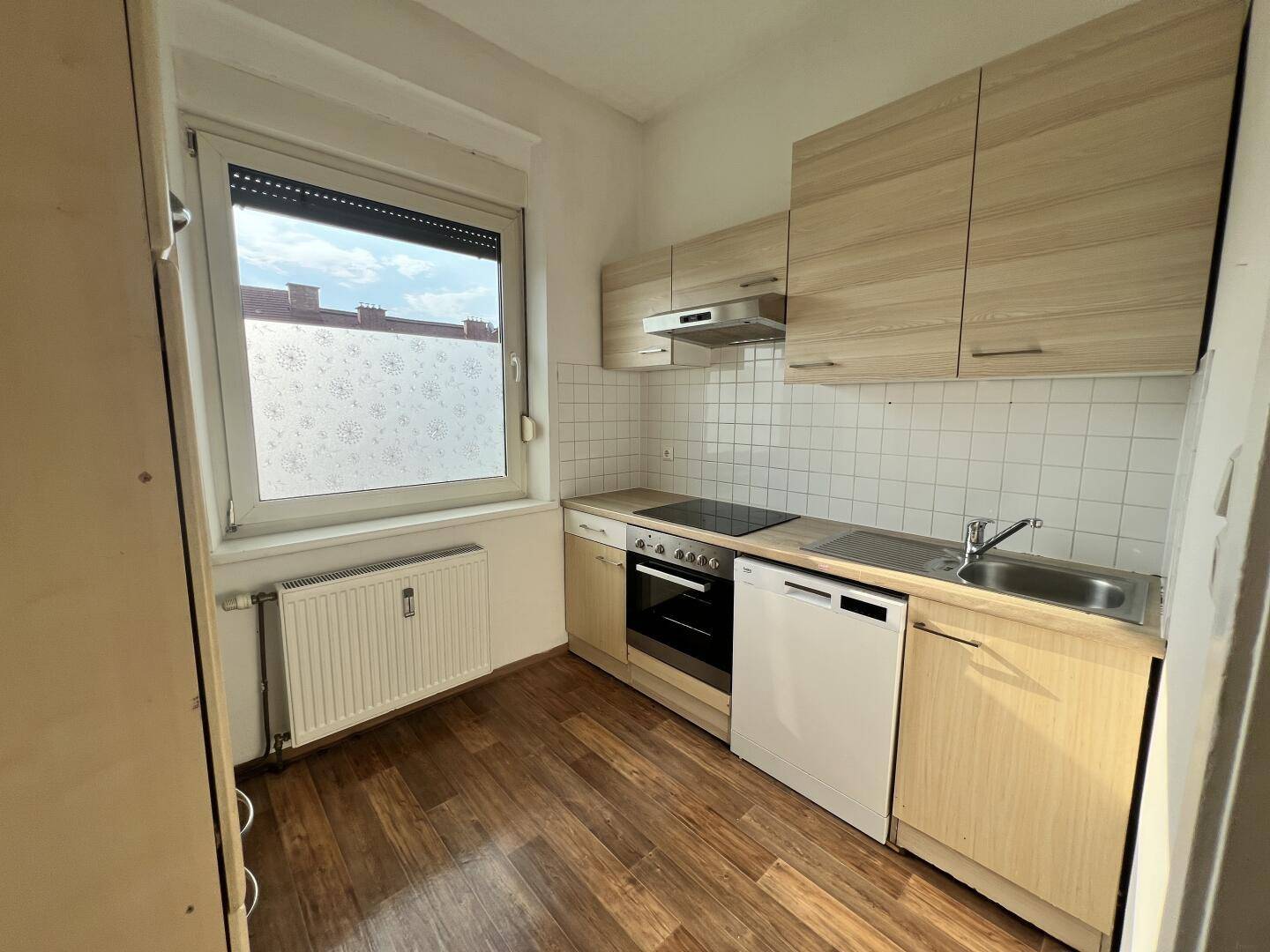 Funktionale Küche mit hellen Holzschränken, Einbaugeräten und einem Fenster für Tageslicht.