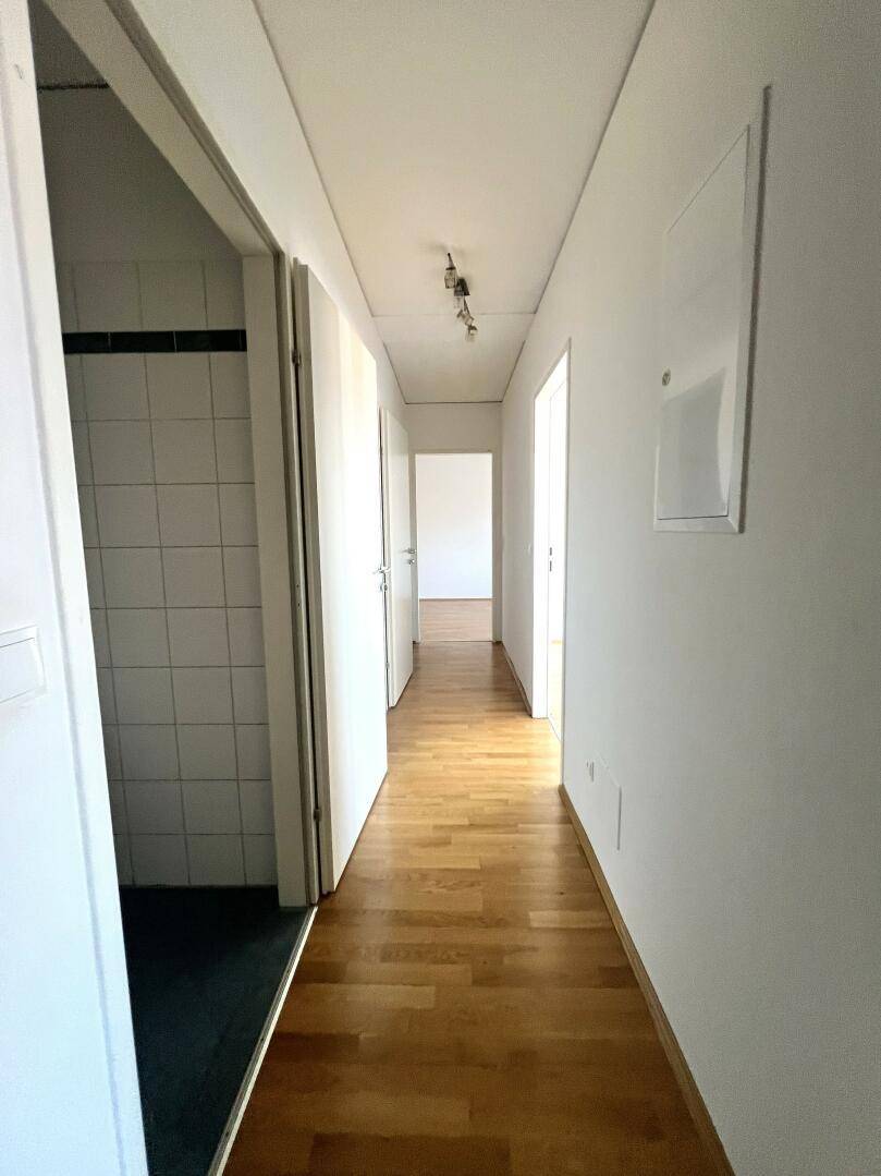 Langer Flur mit Holzboden und Zugang zu Badezimmer und weiteren Zimmern.