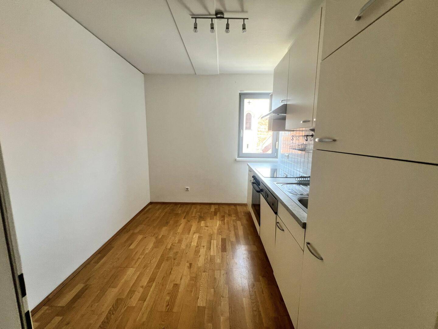 Küche mit einfacher Einbauküche, Fenster und Holzboden.