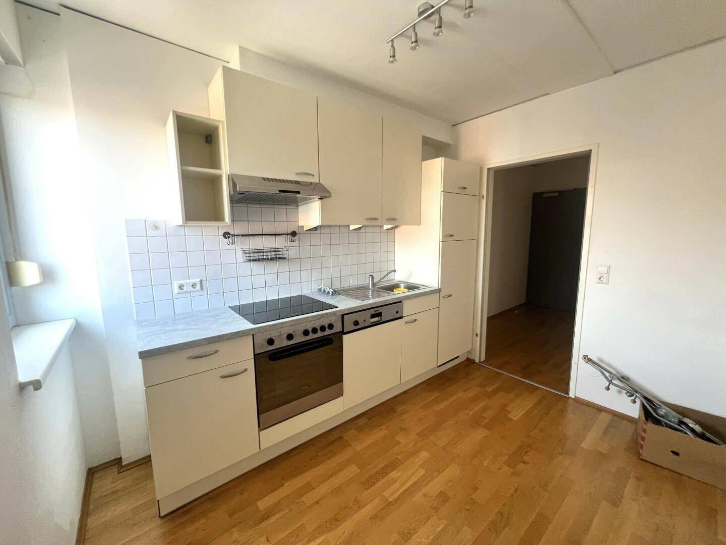 Funktionale Einbauküche mit weißen Oberschränken, Fliesenrückwand und Holzboden.