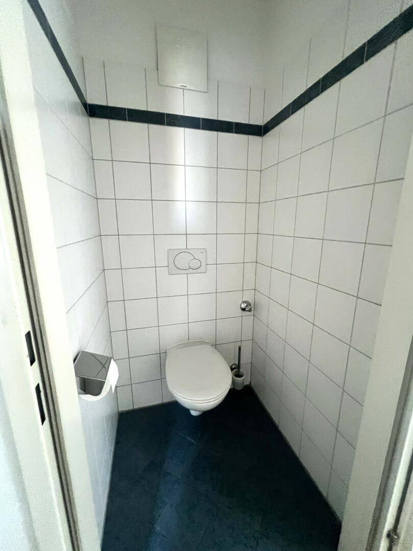 Separate Toilette mit wandhängendem WC, weißen Fliesen und dunklem Boden.