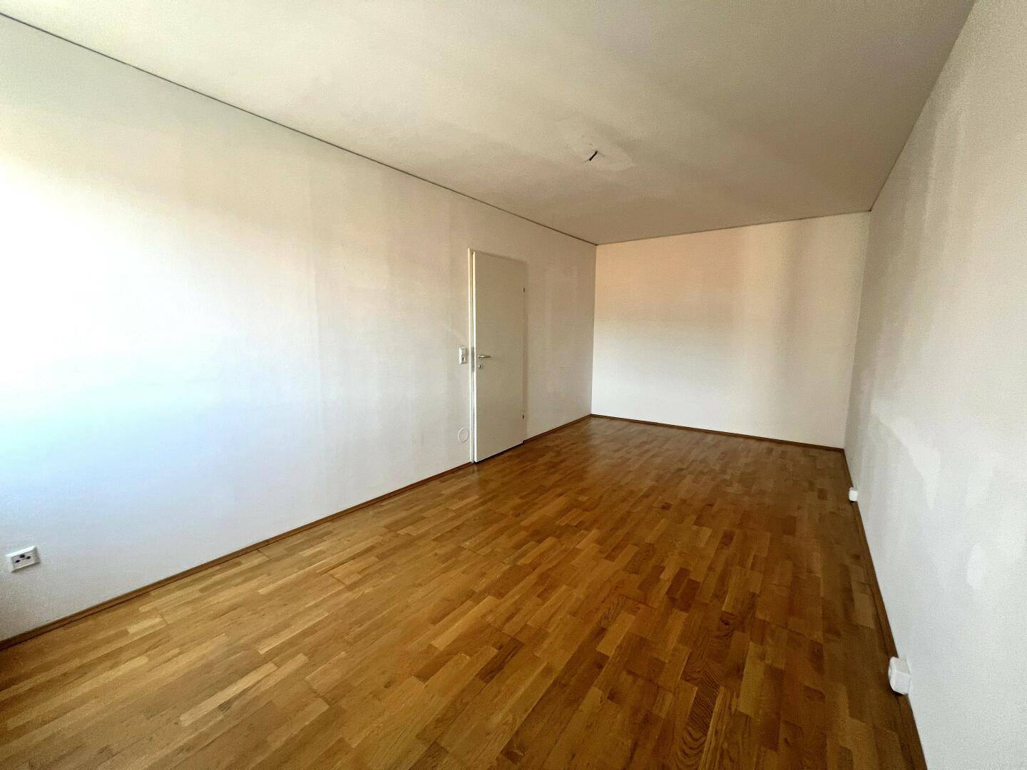 Geräumiges leeres Wohnzimmer mit Holzboden und weißen Wänden.