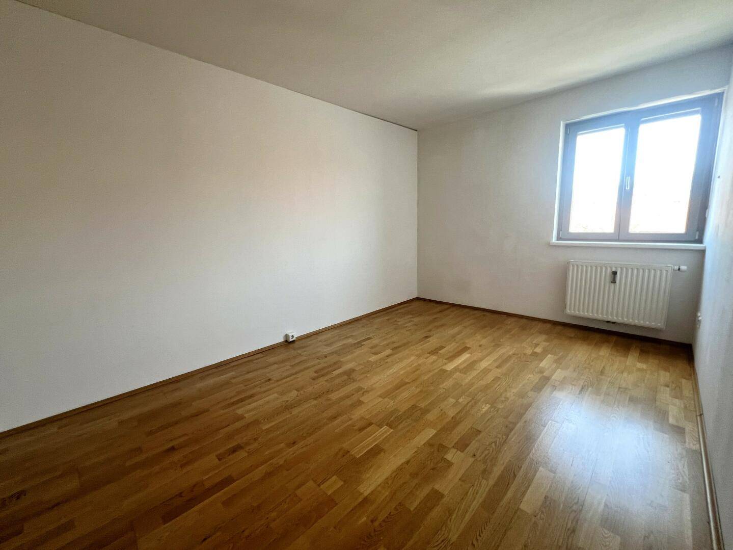 Leeres Wohnzimmer mit Holzboden und einem Fenster, bereit zur individuellen Gestaltung.