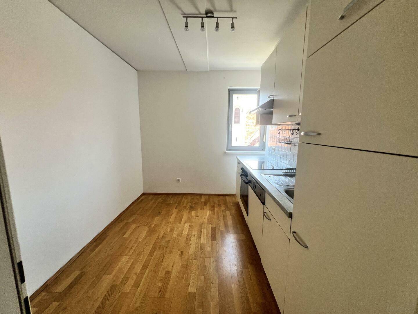 Funktionale Einbauküche mit hellen Schränken und Parkettboden, bereit zur Nutzung.