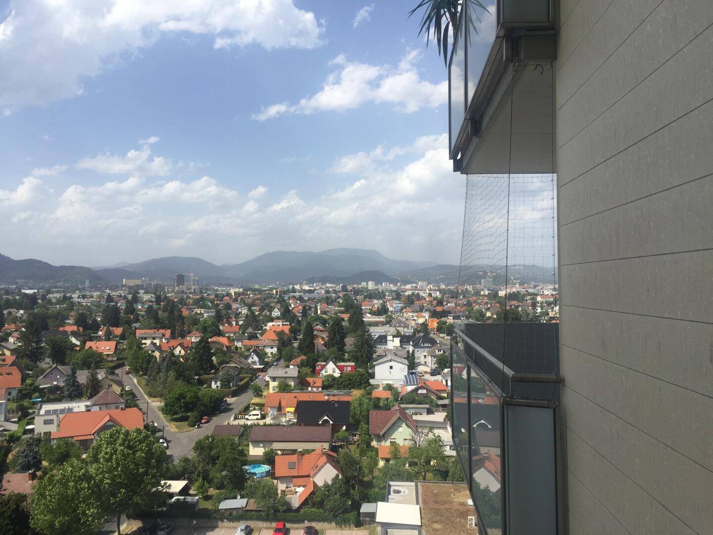 Panoramablick über die Stadt mit Wohngebäuden und grünen Hügeln im Hintergrund an einem sonnigen Tag.