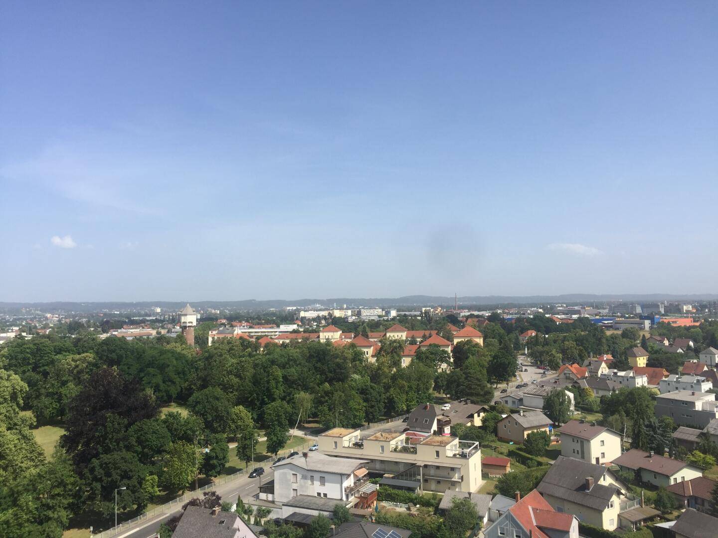 Weitläufiger Blick über die Stadt mit viel Grün und einem Wasserturm unter blauem Himmel.