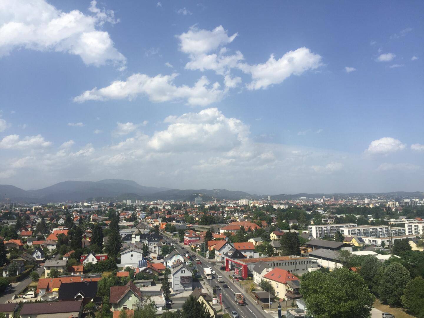 Panoramablick über die Stadt mit Wohngebieten und Bergen im Hintergrund unter blauem Himmel.