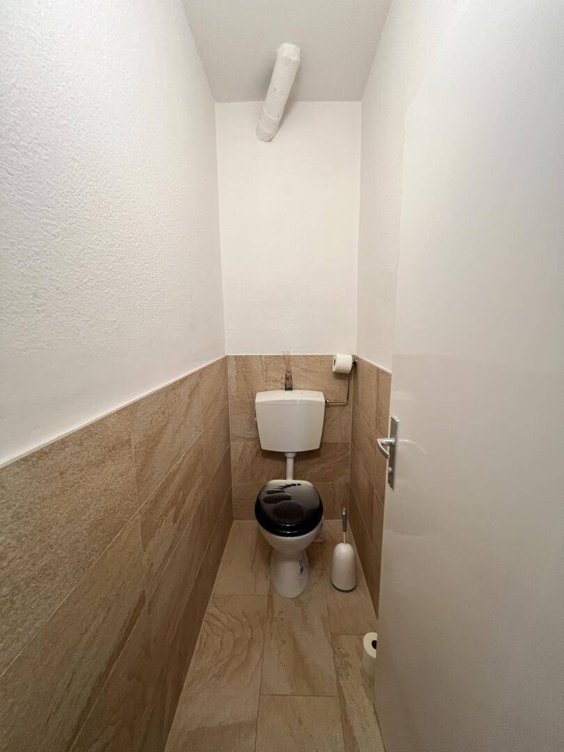 Kleines Gäste-WC mit WC, Fliesenboden und halbhohen Wandfliesen in Beige.