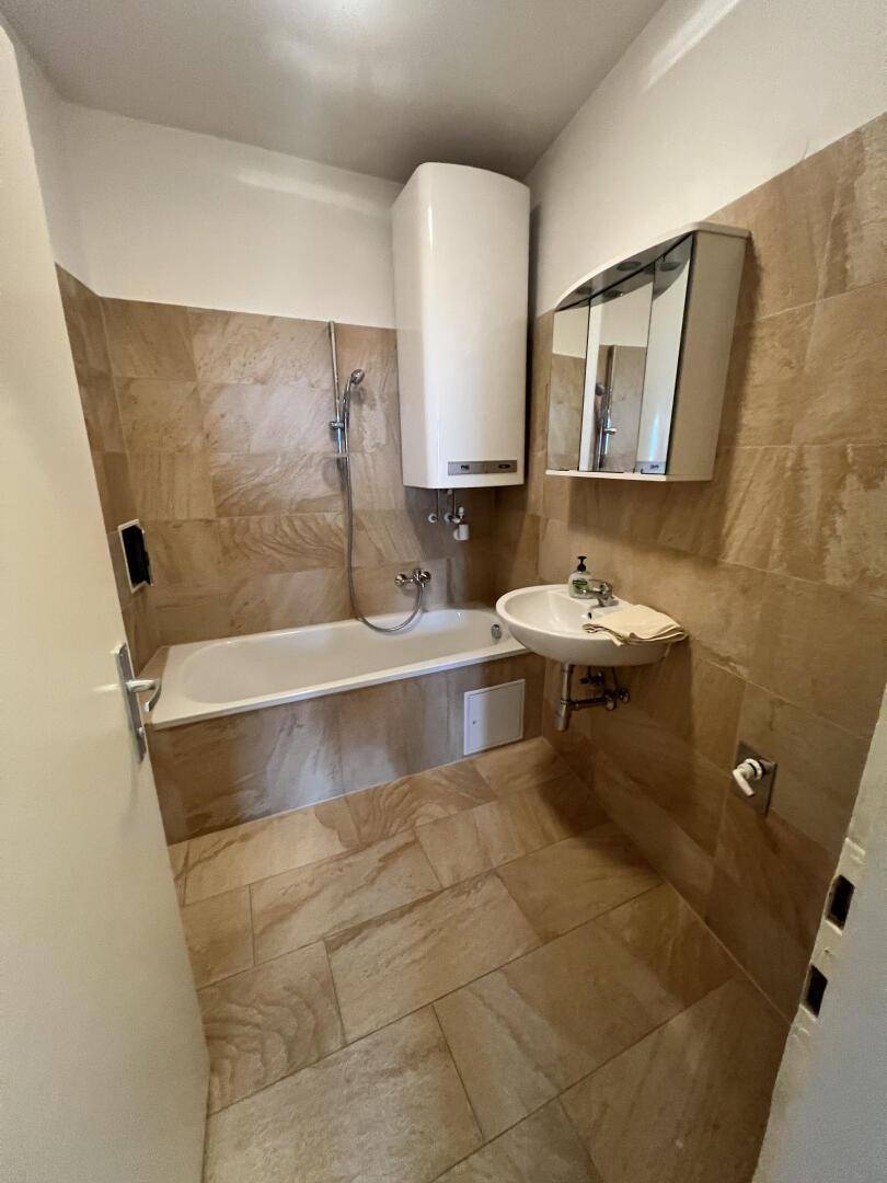 Badezimmer mit Badewanne, Dusche, Waschbecken und beigefarbenen Fliesen an Boden und Wänden.