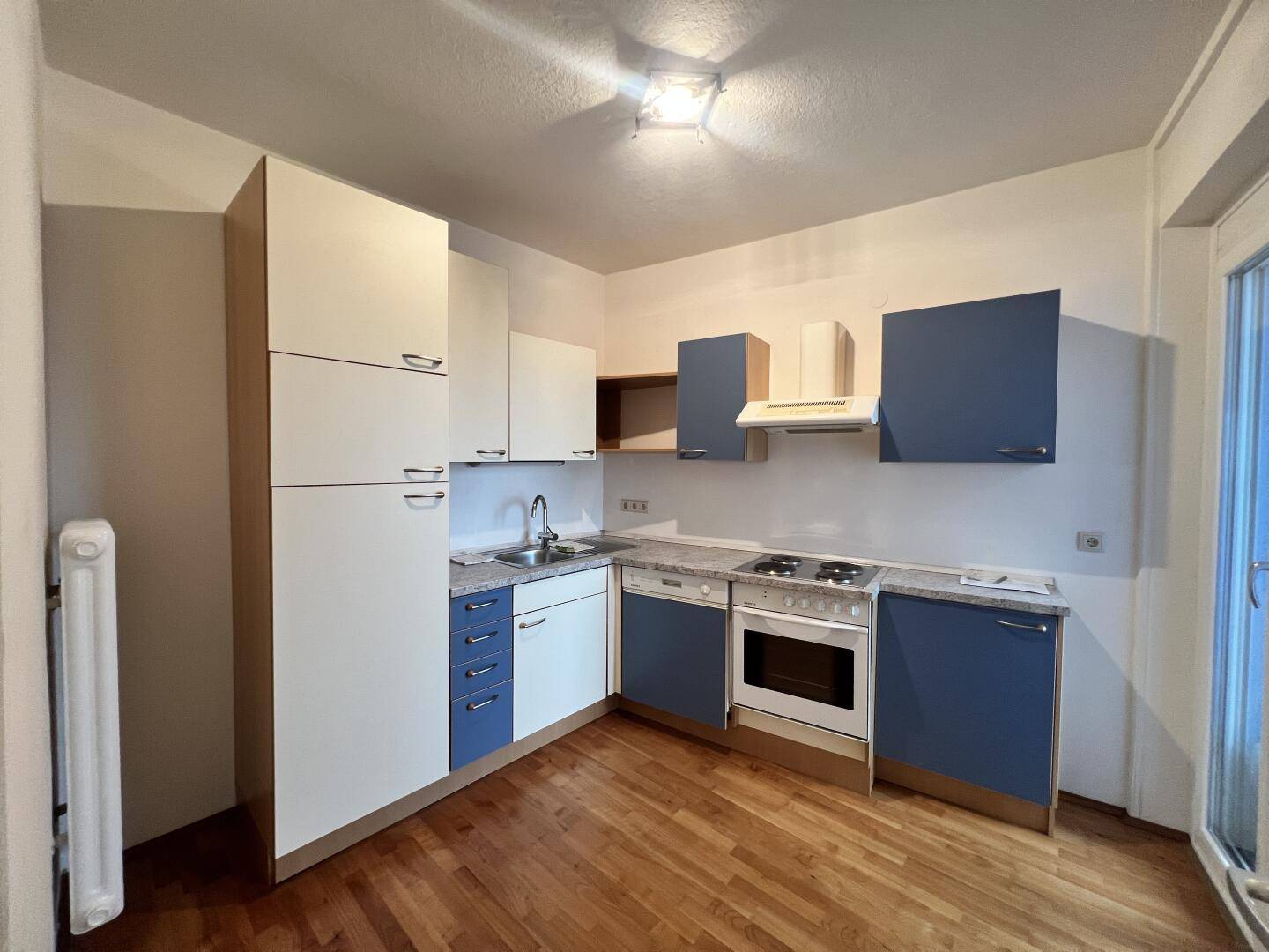 Einbauküche mit blauen und weißen Schränken, Herd und Spüle, mit Zugang zum Balkon.