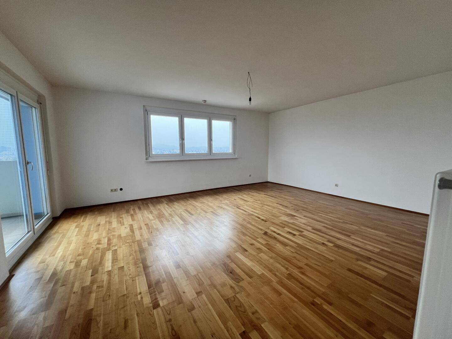 Helles Wohnzimmer mit Parkettboden, großen Fenstern und Zugang zum Balkon.
