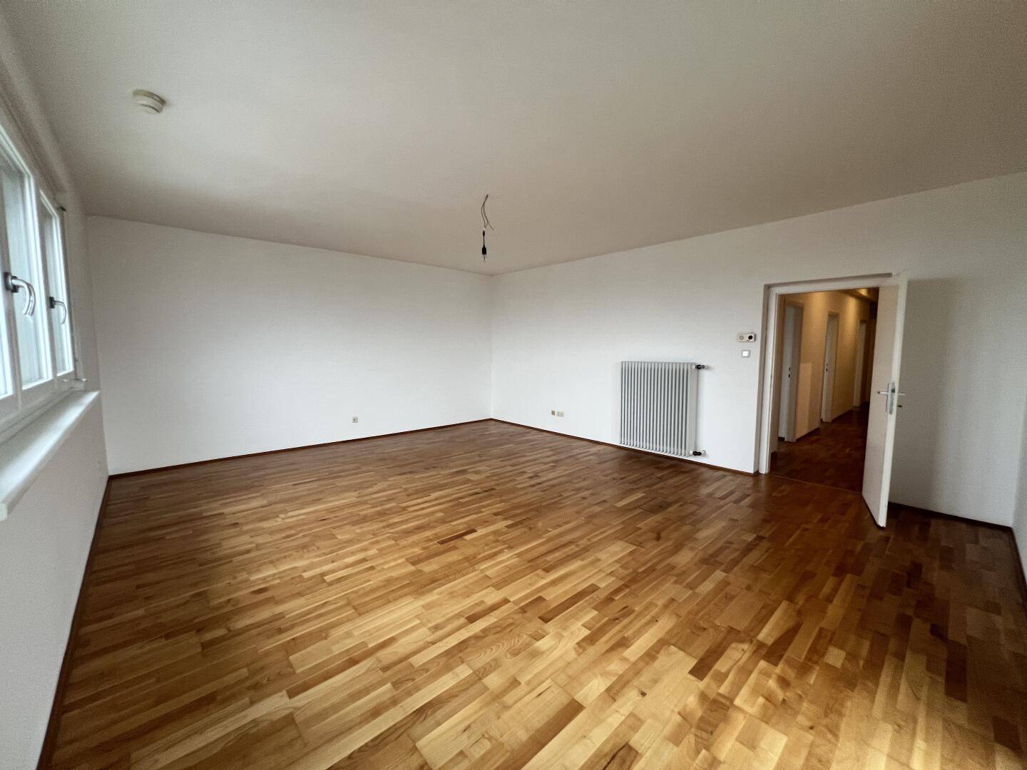 Leeres Wohnzimmer mit Parkettboden, großen Fenstern und Blick auf die Umgebung.