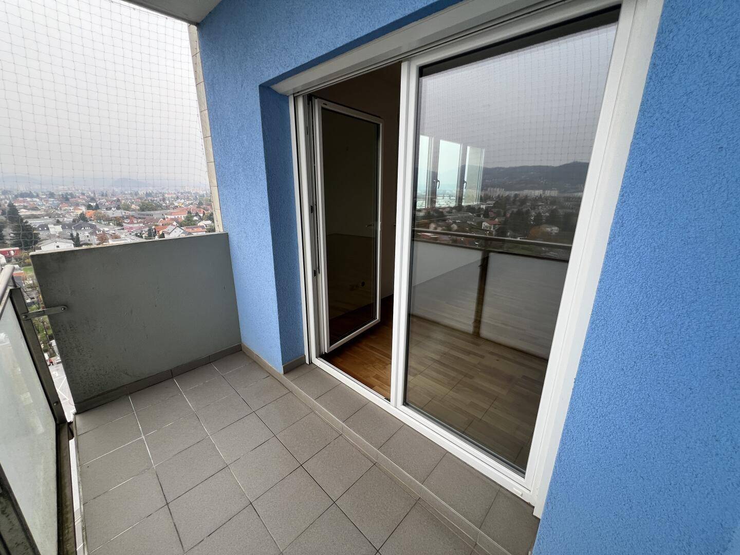 Balkon mit Schiebetür zum Innenraum und Blick auf die Stadt und die Berge.