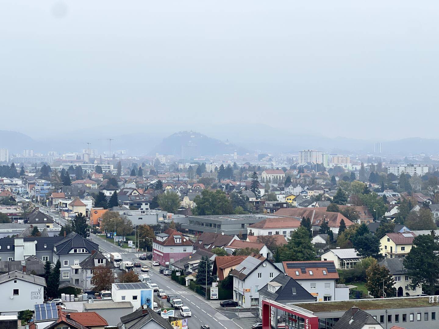 Panoramablick über die Stadt mit Wohngebieten und Bergen im Hintergrund unter bewölktem Himmel.