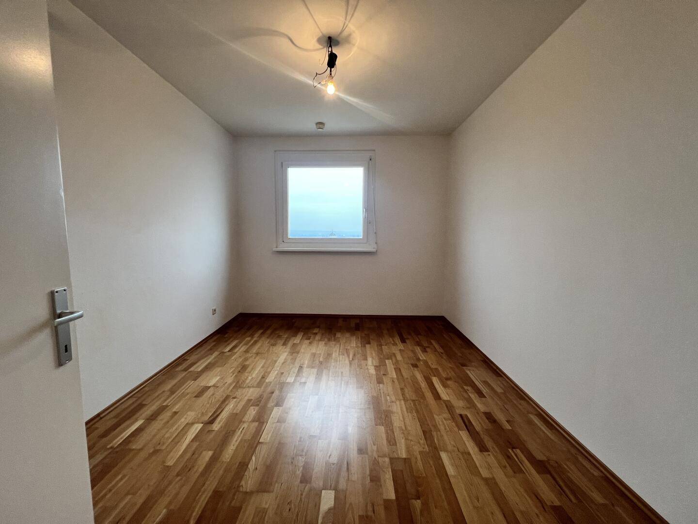 Helles Zimmer mit Parkettboden und einem Fenster, das einen weiten Blick bietet.