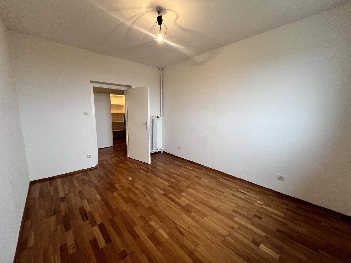 Leeres Zimmer mit Parkettboden und Zugang zu einem Abstellraum.
