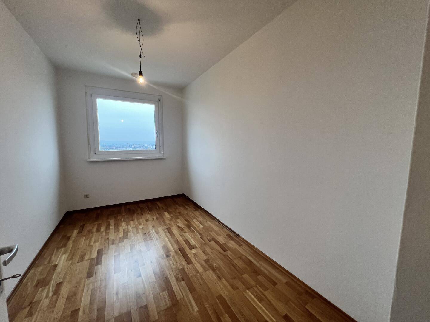 Helles Zimmer mit Parkettboden und einem Fenster, das einen weiten Blick bietet.