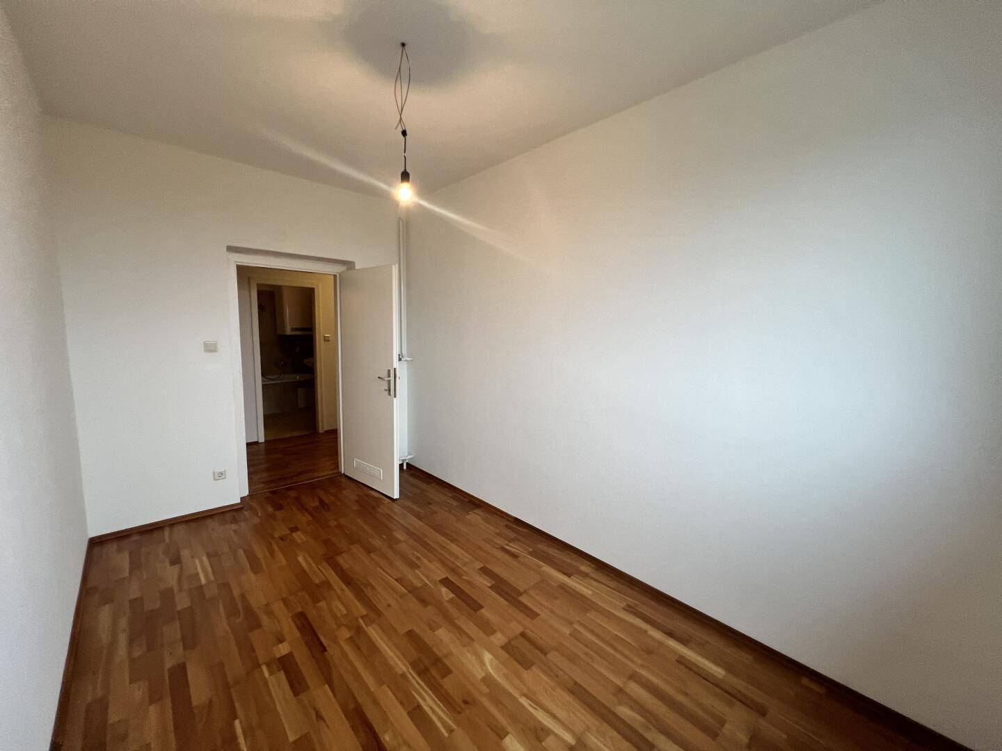 Leeres Zimmer mit Parkettboden und Zugang zu einem weiteren Raum.