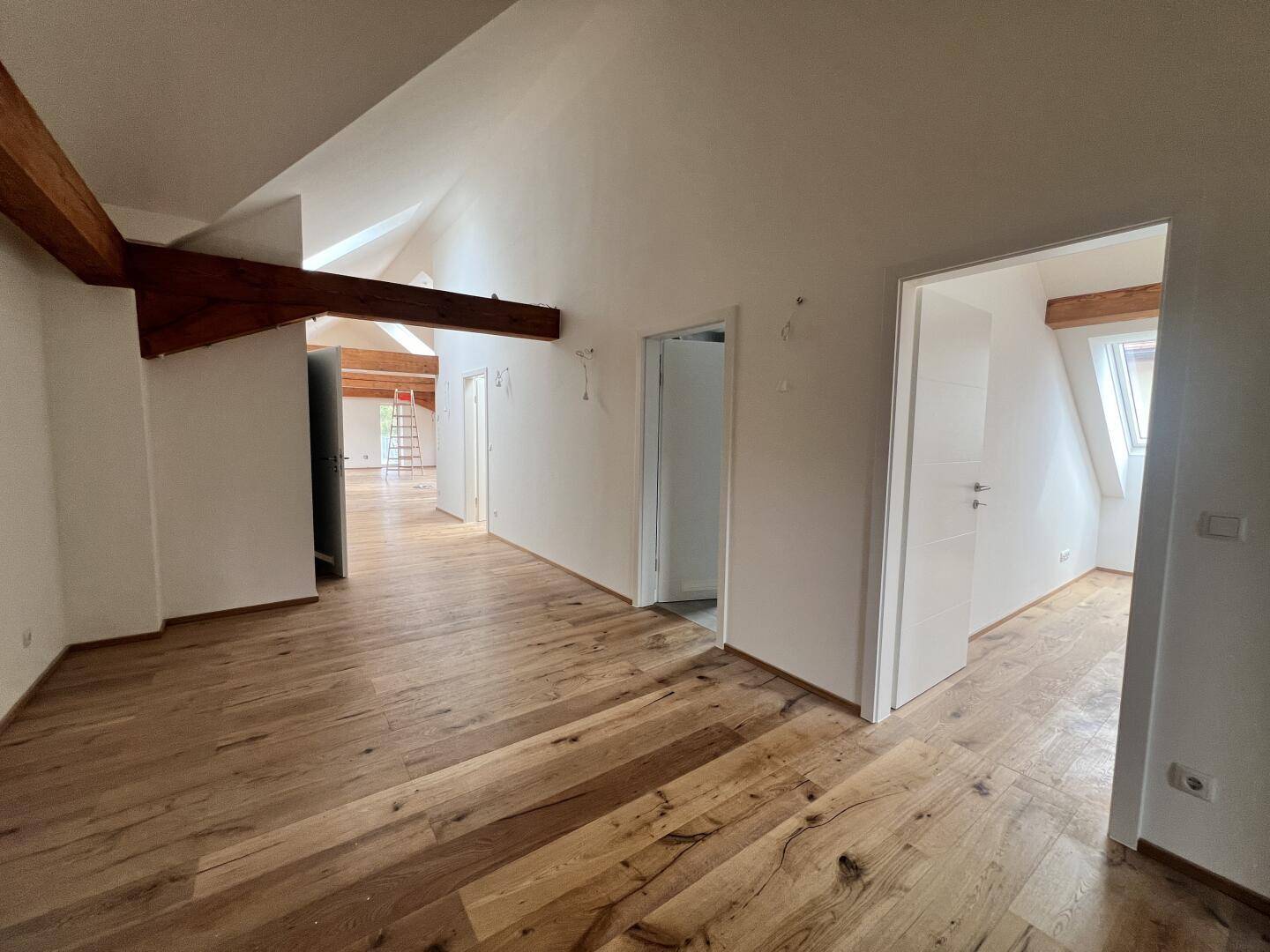 Geräumiges Dachgeschosszimmer mit Holzboden, sichtbaren Balken und Dachschräge.