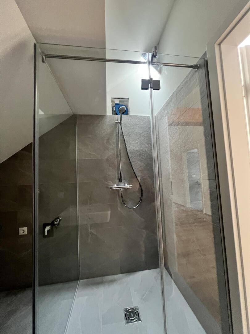 Moderne Glasdusche in einem gefliesten Badezimmer mit Dachschräge.