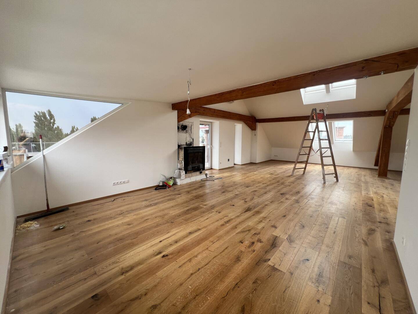 Weitläufiger Wohnbereich mit Holzboden, sichtbaren Balken, Dachfenstern und Kamin.