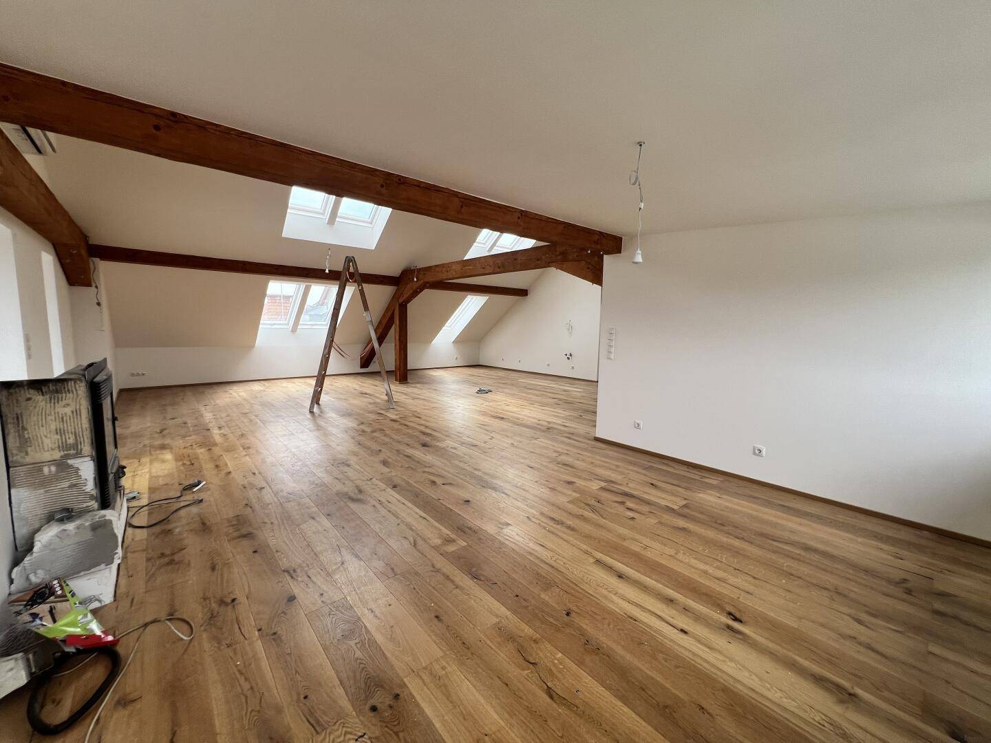 Geräumiges Dachgeschosszimmer mit Holzboden, Kamin und viel natürlichem Licht.