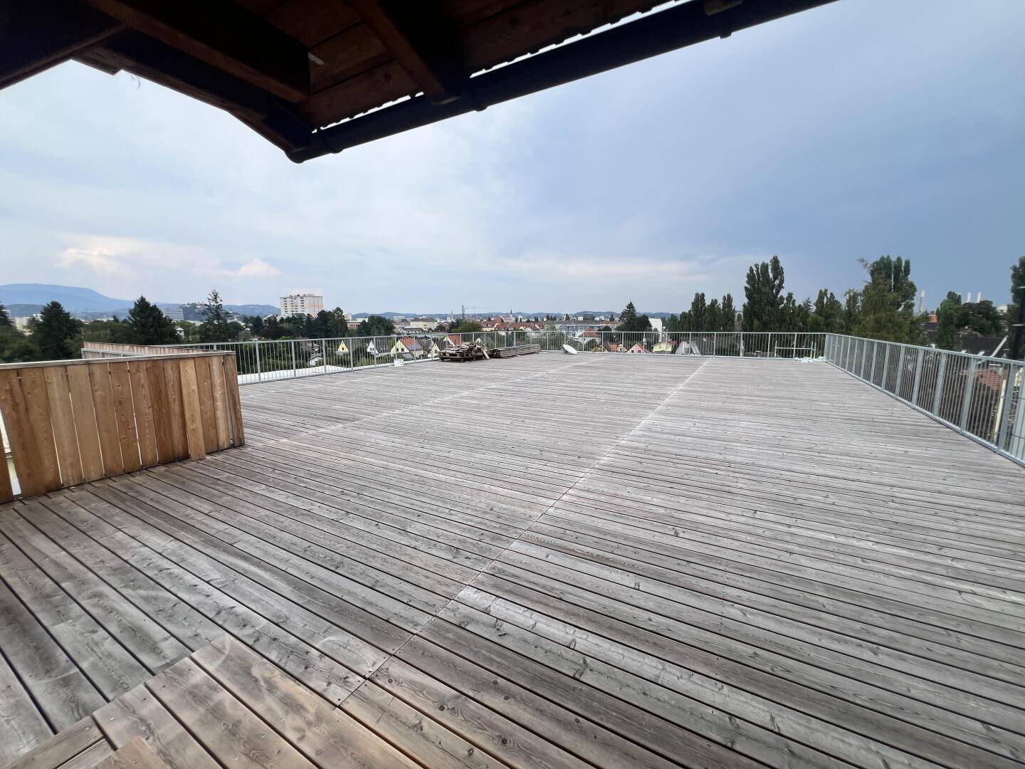 Weitläufige Holzterrasse mit Stadtblick unter bewölktem Himmel, ideal für Entspannung.