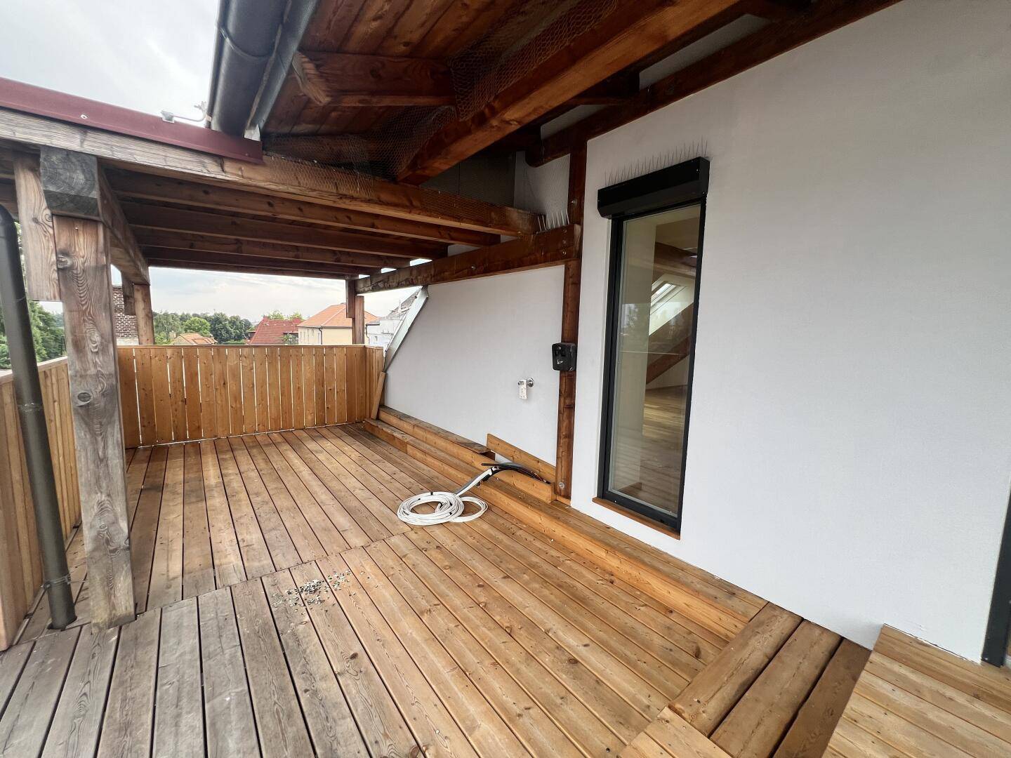 Überdachter Terrassenbereich mit Holzboden, Fenster und Rollladen.