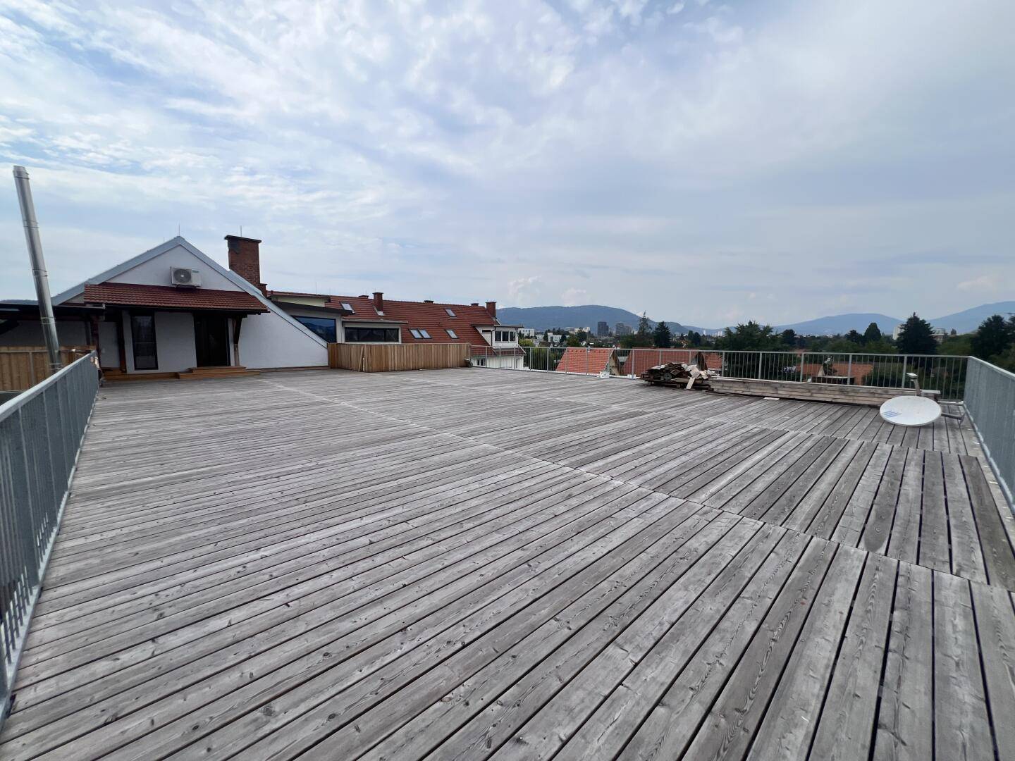 Große Holzterrasse mit weitem Blick über die Umgebung und angrenzende Gebäude.