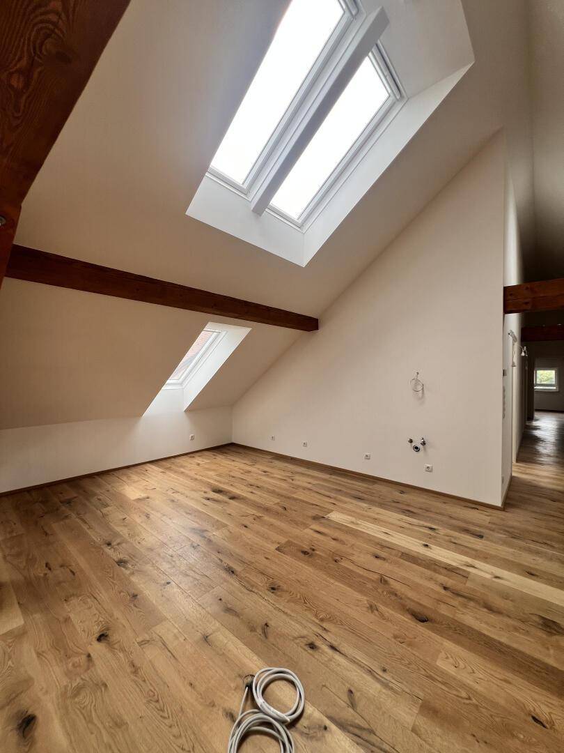 Helles Zimmer mit Holzboden, Dachschräge und zwei großen Dachfenstern.