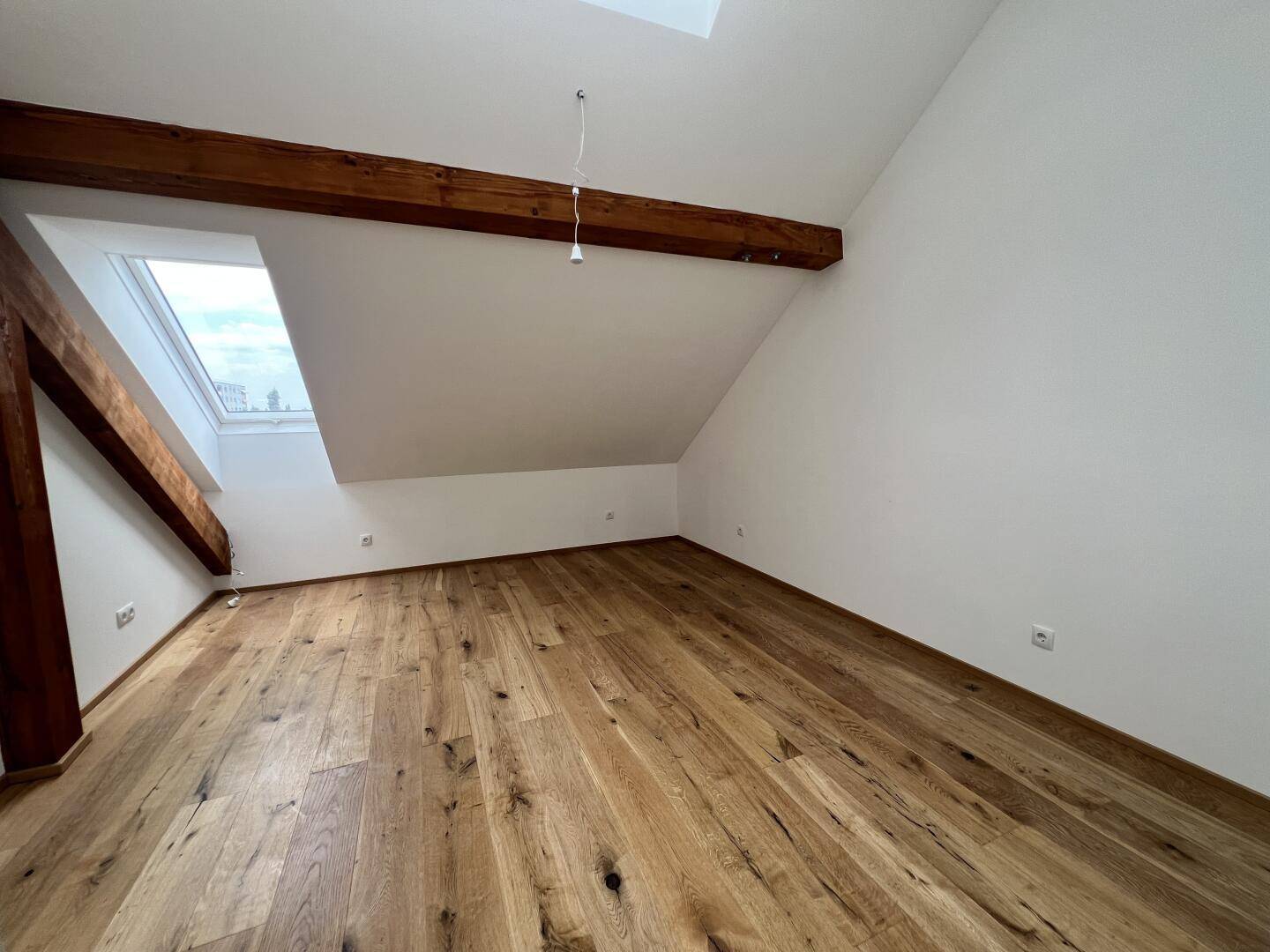 Gemütliches Zimmer mit Holzboden, Dachschräge und einem Dachfenster für natürliches Licht.