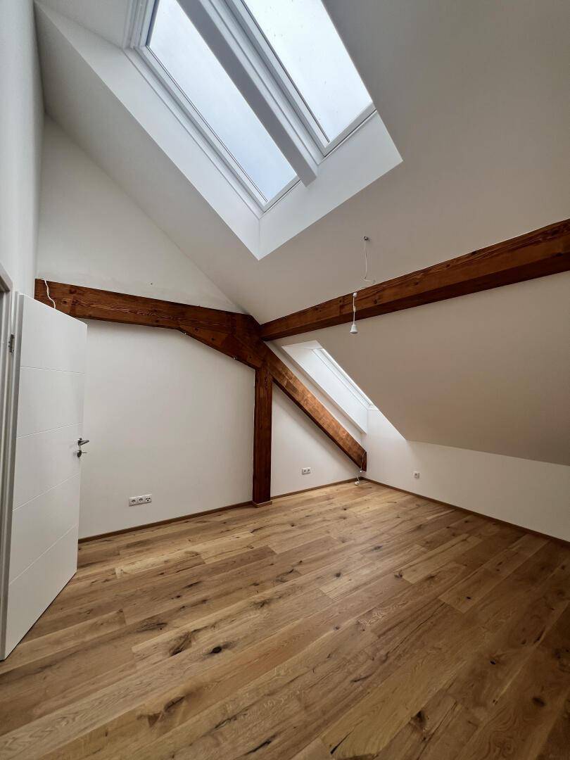 Geräumiges Zimmer mit Holzboden, Holzbalken, Dachschräge und Dachfenstern.