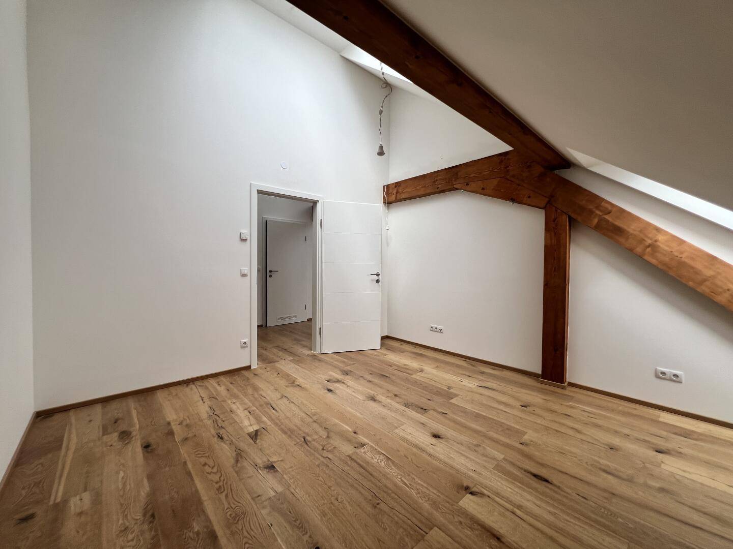 Zimmer mit Holzboden, Dachschräge und weißer Tür, bereit zur individuellen Gestaltung.