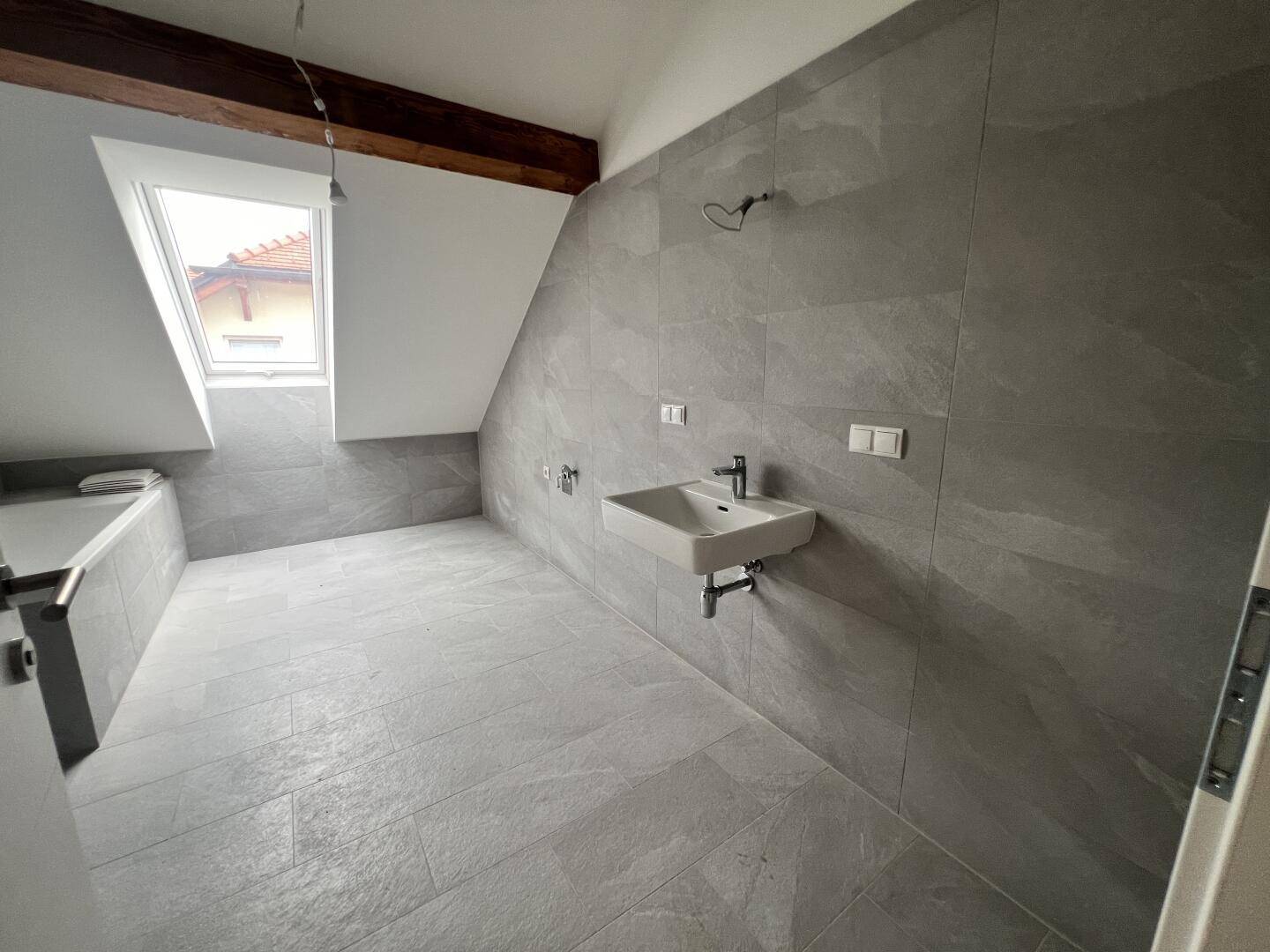 Modernes Badezimmer mit grauen Fliesen, Waschbecken, Badewanne und Dachfenster.