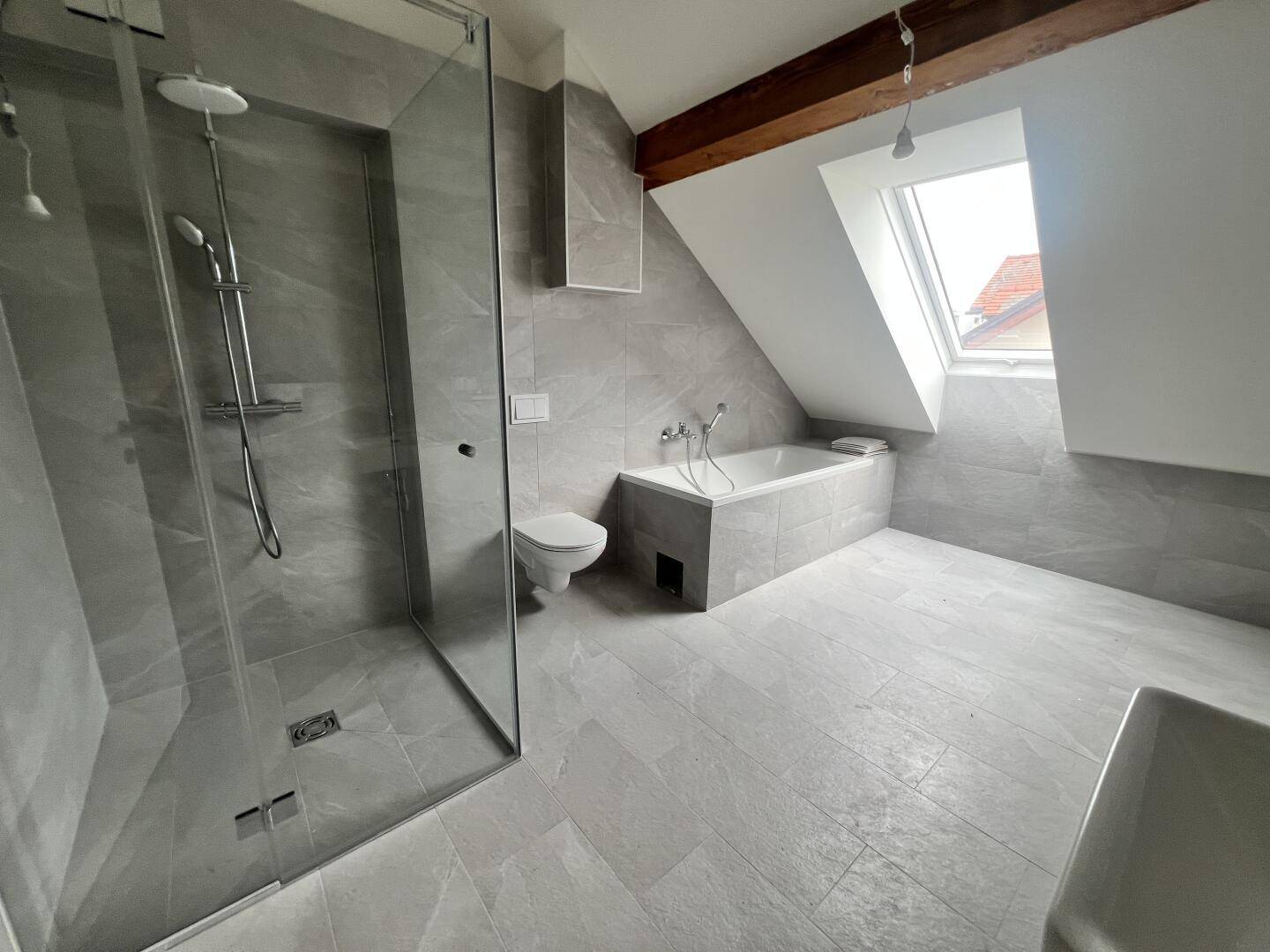Geräumiges Badezimmer mit Badewanne, Dusche, Wand-WC und Dachfenster.