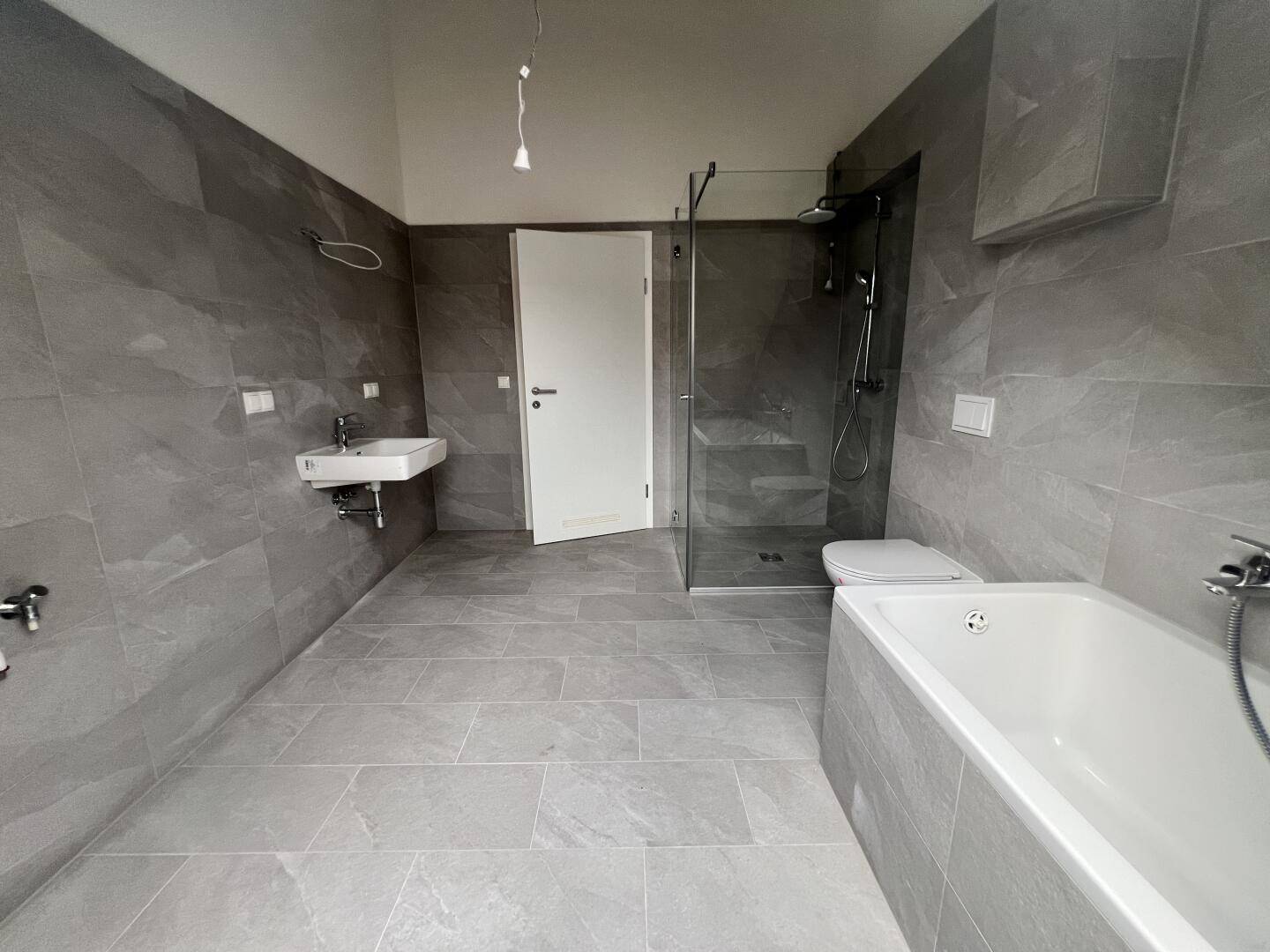 Modernes Badezimmer mit Badewanne, Glasdusche, Wand-WC und Waschbecken.