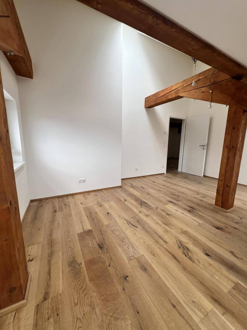 Helles Zimmer mit Holzboden, sichtbaren Balken und Dachschräge, ideal für ein Schlafzimmer.